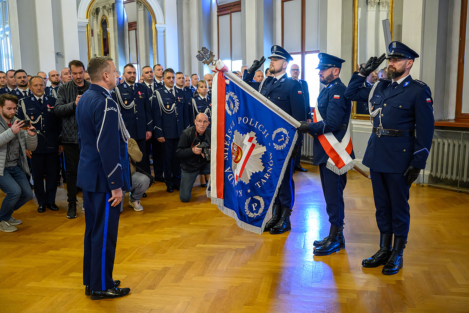 Przedstawiciele policji ze sztandarem salutują witając nowego komendanta